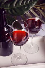 Two glasses with red grape wine with bottle on the background. Romantic dinner concept.