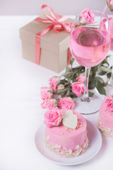 Mini small cake with pink glaze, beautiful roses, cup of coffee, gift box on the white table.