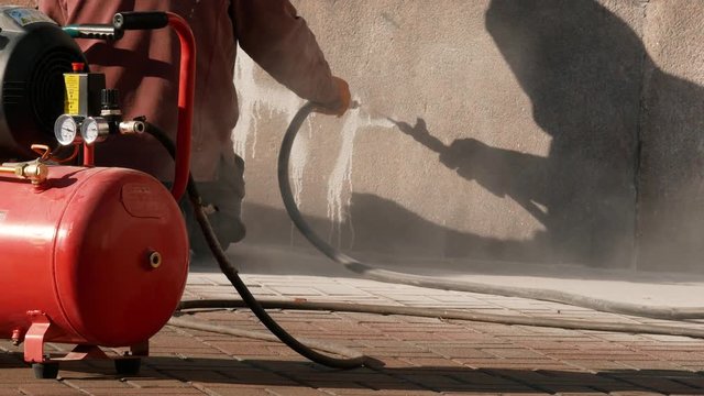 Worker removing graffiti with high pressure cleaner. Cleaning wall using sandblaster gun. Professional cleaning services 4k
