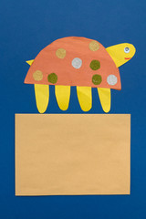 brown empty sheet of paper and applique of a funny handmade turtle on a blue background