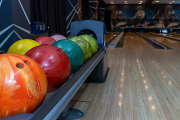 Bowling balls lie in a holder in a line. Colored balls and bowling lane.