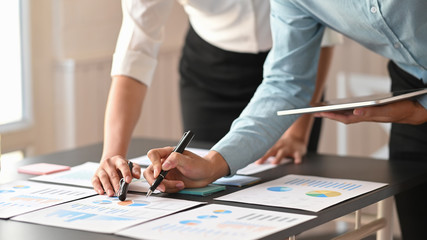 Business development team talking/planning about their business by using computer tablet and paper work while standing at the modern meeting table with comfortable meeting room as background.