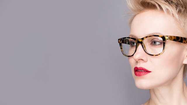 portrait of a young woman, blonde, glasses over grey background