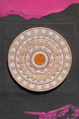 Rosace de pierre colorée décorative sur mur noir de maison avec graphismes artistiques roses.