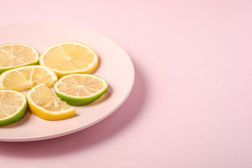 Fototapeta na wymiar Fresh tasty lemon and lime citrus fruits slices on pink plate, minimal background isolated, angle view