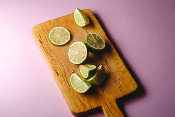 Fresh tasty lime citrus fruits slices on wooden cutting board, minimal pink background isolated, angle view