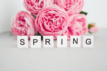 wooden letters spring on a background of pink peonies 