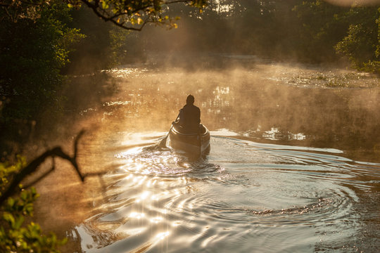 Mann sitzt im Kanu und Paddelt  zum Sonnenaufgang auf einem Fluss