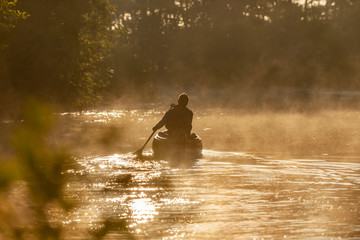 Mann sitzt im Kanu und Paddelt  zum Sonnenaufgang auf einem Fluss