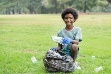 African American boy volunteer smiling picking up plastic bottles into a black garbage bag, help garbage collection charity environment