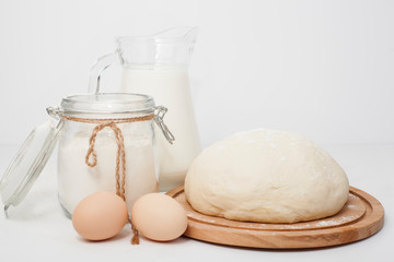 Dough close-up next to milk, flour and eggs, on a white background. Concept of making pastries, bread, pie recipes.