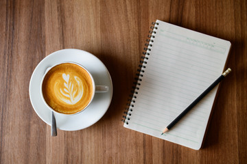 cup of latte art coffee with blank notebook and pencil