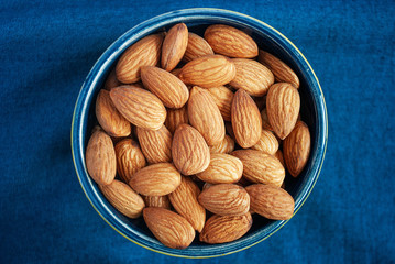 Dried almonds in a small bowl on the blue background.