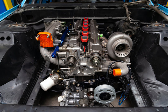 Powerful tuned gasoline engine with a turbocharger and a charger in the engine compartment of an automobile with an open hood and a turbine in a car repair and improvement workshop.