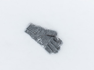 single glove lying in a white snowdrift of snow. gray knitted glove. Winter background