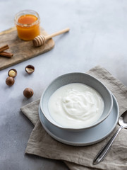 natural white yogurt in a bowl, macadamia nuts and a jar of honey. healthy food. gray concrete background. vertical image