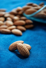 Dried almonds close up on the blue surface. Scattered almonds from bowl on the blue surface.