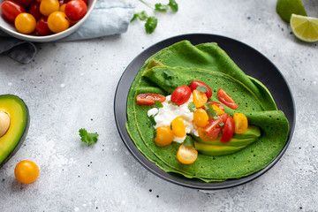 crepes with spinach, avocado, cottage cheese and colorful cherry tomatoes on a dark plate. delicious breakfast or brunch. gray concrete background. horizontal image.