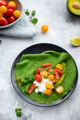 crepes with spinach, avocado, cottage cheese and colorful cherry tomatoes on a dark plate. Mediterranean Kitchen. Gray background. vertical image, top view