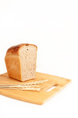 Half a loaf of rye-wheat bread on a cutting board with ears of wheat. Bread, food