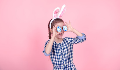 Portrait of a cute little girl with Easter eggs on a pink background.