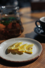 slices of lemon lie on a white plate, next to a teapot of black tea and a mug and saucer