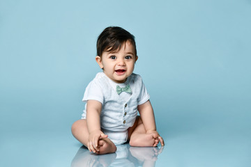 Baby boy in white bodysuit as a vest with bow-tie, barefoot. He smiling, sitting on the floor...