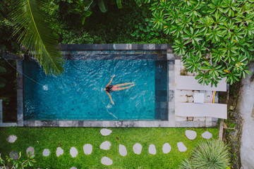 Beautiful girl relaxing outdoor in her garden with swimming pool. Summer concept about lifestyle,beauty, vacations and real estates. Aerial drone view