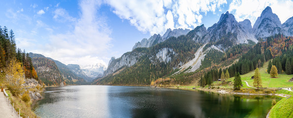 Famous Lake Gosau and Gosaukamm with Mount Dachstein. The sun is about to hide behind the high peaks while autumn is about to settle in with all the vibrant colors around the lake and hills.