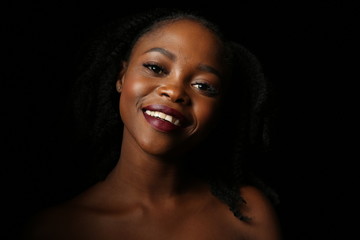 Portrait of a young beautiful African woman with thick black curly hair on an isolated black background. The woman smiles