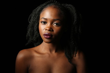 Portrait of a young beautiful African woman with thick black curly hair on an isolated black background