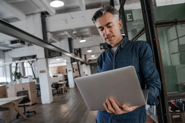 Serious concentrated adult man working on laptop computer in creative agency office. Successful business strategy plan concept. Confident office worker indoor in coworking space. People lifestyle