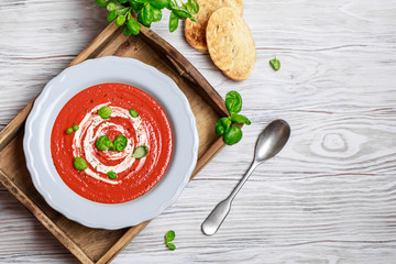 Bowl of tomato soup with a basil on wooden background