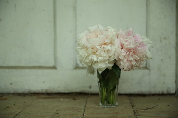A bouquet of pink peonies stands in a glass vase against a white wooden door
