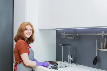 teenager girl  in purple rubber gloves washes dishes in kitchen