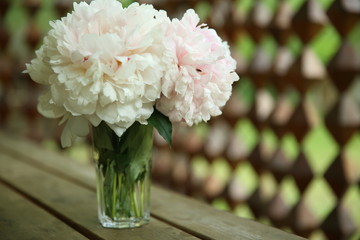 A bouquet of pink peonies stand in a glass vase against the background of a wooden table and a...