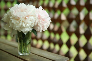 A bouquet of pink peonies stand in a glass vase against the background of a wooden table and a...