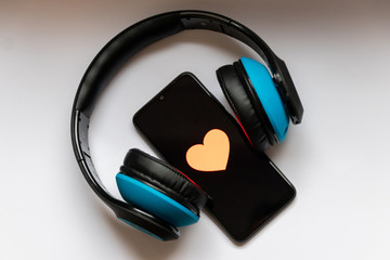 Schwarzes Smartphone mit Herz zum Valentinstag und blauem Funkkopfhörer zeigt Liebe zur Musik und...