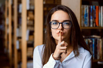 Student woman making silence gesture in a library, preventing from making loud noise in the reading...