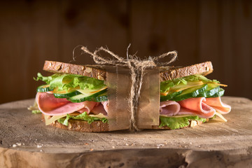 sandwich with meat, salad, cucumbers on a wooden surface