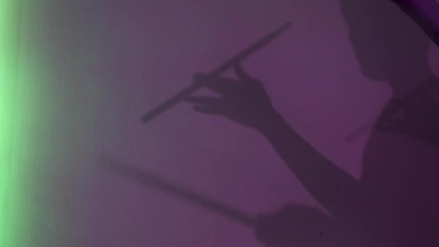 Side view of young drummer silhouette with drum stick on purple wall background. Concept. Male shadow pretending to drum under neon light of lamps, music and art concept.