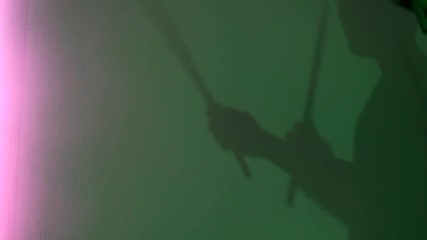 Side view of young drummer silhouette with drum stick on green wall background. Concept. Male shadow pretending to drum under neon light of lamps, music and art concept.