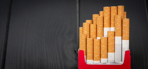 Open pack of cigarettes with cigars coming out on gray wooden background