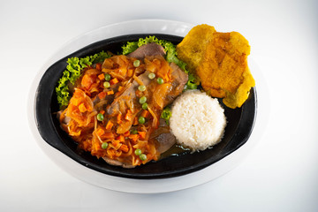 Tongue in sauce with rice, banana fries  on black dish typical colombian food