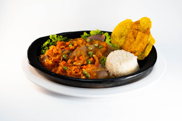 Tongue in sauce with rice, banana fries  on black dish typical colombian food