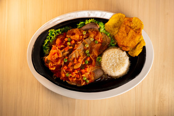 Tongue in sauce with rice, banana fries  on black dish typical colombian food