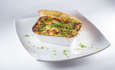 Chicken lasagna with garlic bread, baked in aluminum plate, white background
