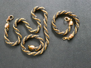 Necklace and bracelet. Cord chain and cord bracelet with lobster clasp, costume jewelry, gold jewelry, cord pattern, black-gold, Close up, black background.