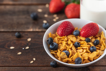 Granola chips with blueberries and raspberries in white bowl in dark wooden desk.