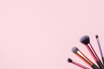 Set of different makeup brushes on a pink background. Flat lay top view copy space
